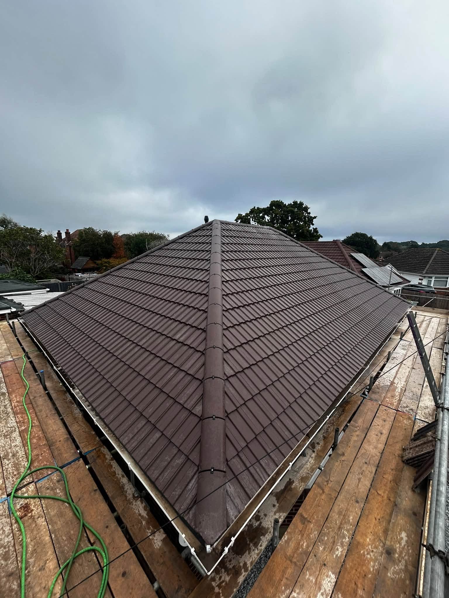 Finished dark brown tiled hipped roof with a dry-fixed hip after a full re-roof in Kinson